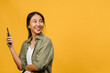 © tirachard - Young Asia lady using phone with positive expression, smiles broadly, dressed in casual clothing feeling happiness and stand isolated on yellow background. Happy adorable glad woman rejoices success.