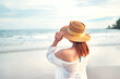 © oatawa - Summer beach vacation concept, Young woman with hat relaxing with her arms raised to her head enjoying looking view of beach ocean on hot summer day, copy space.