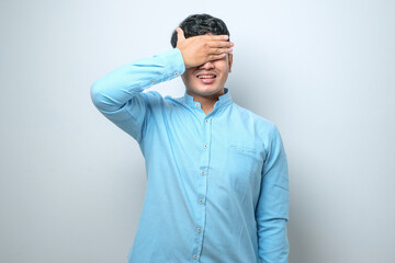 Wall Mural - Young asian man wearing casual clothes smiling and laughing with hand on face covering eyes for surprise.