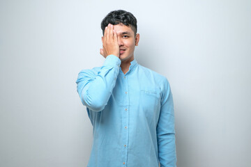 Wall Mural - Young asian man wearing casual shirt covering one eye with hand confident smile on face and surprise emotion.