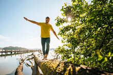 Mature Man Balancing On Fallen Tree At Lakeshore