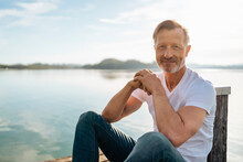 Smiling Mature Man Sitting Hands Clasped By Lake