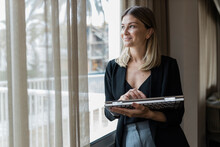 Happy Businesswoman Holding Laptop Looking Through Window At Hotel