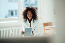 Smiling Female Doctor With Curly Hair Pointing At Tablet PC