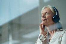 Smiling Senior Woman With Eyes Closed Listening Music Through Wireless Headphones