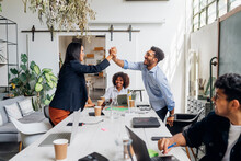 Happy Businessman And Businesswoman Giving High-five Over Desk In Office