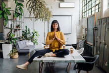 Businesswoman Meditating With Hands Clasped On Desk At Workplace