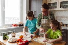 Mother Assisting Daughters To Prepare Pizza In Kitchen At Home