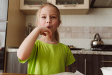Smiling Girl Licking Finger In Kitchen At Home