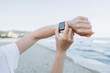 © Westend61 - Hand of woman using smart watch at beach