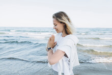 Happy Woman With Hands Clasped Standing In Front Of Sea