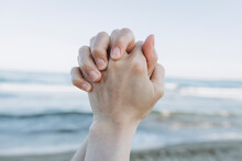 Hands Clasped In Front Of Sea At Beach
