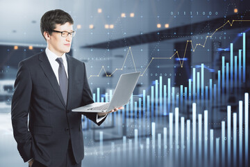 Poster - businessman using laptop with abstract glowing and growing business graph hologram on blurry office interior background. Planning and strategy, stock market, business growth, progress