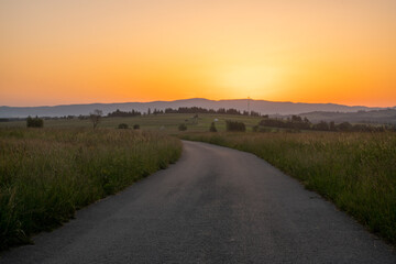 Wall Mural - road running through a mountain meadow towards the rising sun