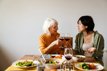 Mature two women drinking wine and talking while having lunch together