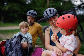 Wall Mural - Young family with little children resting after bike ride, sitting on grass in park in summer.