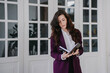 © Iona - Exhausted brunette businesswoman holding notebook, planning her week wearing violet suit. Tired student looking at her agenda in diary. Overloaded lawyer holding law book. Business and finance.
