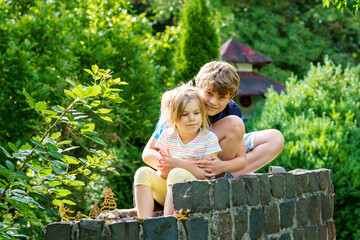 Wall Mural - Portrait of adorable brother and sister smile and laugh together while sitting outdoors. happy lifestyle kids. School boy and preschool girl, bonding, family.