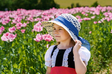 Wall Mural - Little preschool girl in poppy field. Cute happy child in red riding hood dress play outdoor on blossom flowering meadow with pink poppies. Leisure activity in nature with children.