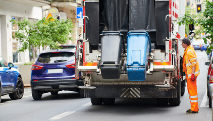 garbage and waste removal services. worker loading waste bin into truck at city