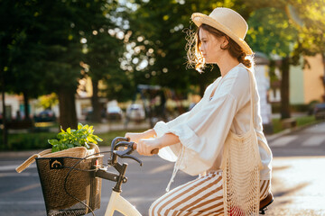 Happy young girl in summer clothes riding bicycle at the city street outdoor. Bicycle and ecology lifestyle concept.