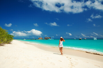 Sticker - Fashion woman walking on the beach. Happy island lifestyle. White sand, blue cloudy sky and crystal sea of tropical beach. Vacation at Paradise. Ocean beach relax, travel to islands