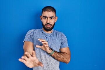 Sticker - Middle east man with beard standing over blue background disgusted expression, displeased and fearful doing disgust face because aversion reaction.