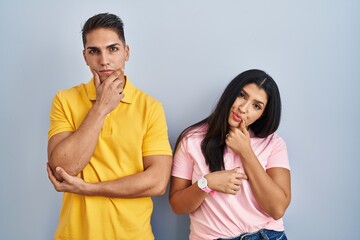 Sticker - Young couple standing over isolated background looking confident at the camera smiling with crossed arms and hand raised on chin. thinking positive.