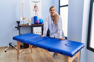 Wall Mural - Young blonde woman wearing physiotherpist uniform standing at physiotherapy clinic