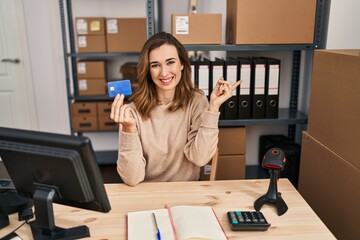 Poster - Young woman working at small business ecommerce holding credit card smiling happy pointing with hand and finger to the side