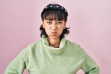 Poster - Young beautiful woman standing over pink background puffing cheeks with funny face. mouth inflated with air, crazy expression.