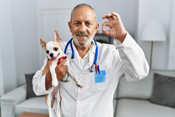 Sticker - Mature veterinarian man checking dog health doing ok sign with fingers, smiling friendly gesturing excellent symbol