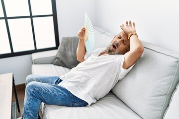 Canvas Print - Senior grey-haired man using handfan at home