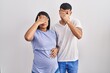 Young hispanic couple expecting a baby standing over background covering eyes with hand, looking serious and sad. sightless, hiding and rejection concept