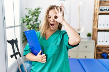 Canvas Print - Young caucasian woman working at pain recovery clinic doing ok gesture shocked with surprised face, eye looking through fingers. unbelieving expression.