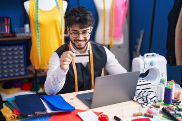 Wall Mural - Young hispanic man tailor using laptop and credit card at sewing studio