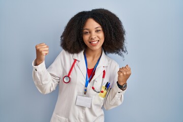 Wall Mural - Young african american woman wearing doctor uniform and stethoscope very happy and excited doing winner gesture with arms raised, smiling and screaming for success. celebration concept.