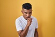 © Krakenimages.com - Young hispanic man standing over yellow background feeling unwell and coughing as symptom for cold or bronchitis. health care concept.