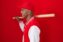 Young Hispanic Man Playing Baseball Holding Bat Looking To Side, Relax Profile Pose With Natural Face And Confident Smile.