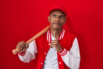 Poster - Young hispanic man playing baseball holding bat thinking concentrated about doubt with finger on chin and looking up wondering