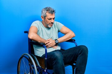 Poster - Handsome middle age man with grey hair sitting on wheelchair with hand on stomach because indigestion, painful illness feeling unwell. ache concept.