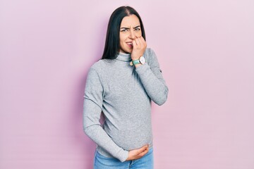 Poster - Beautiful woman with blue eyes expecting a baby, touching pregnant belly looking stressed and nervous with hands on mouth biting nails. anxiety problem.