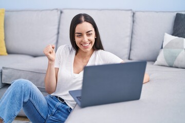 Canvas Print - Young brunette woman using laptop at home screaming proud, celebrating victory and success very excited with raised arm