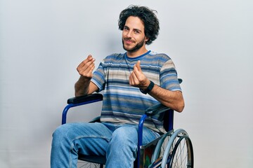 Wall Mural - Handsome hispanic man sitting on wheelchair doing money gesture with hands, asking for salary payment, millionaire business