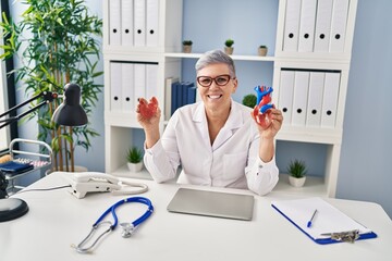 Sticker - Middle age woman wearing doctor uniform holding heart ventricles at clinic