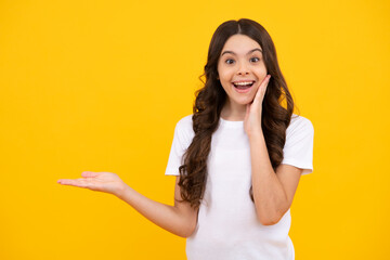 Happy teenager, positive and smiling emotions of teen girl. Close-up portrait of her she nice cute attractive cheerful amazed girl pointing aside on copy space isolated on yellow background.