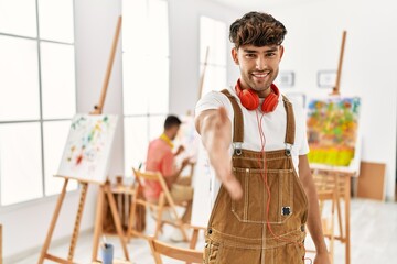 Poster - Young hispanic man at art studio smiling friendly offering handshake as greeting and welcoming. successful business.