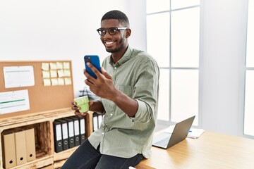 Wall Mural - Young african american man using smartphone drinking coffee at office