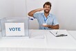 © Krakenimages.com - Young handsome man at political election sitting by ballot gesturing with hands showing big and large size sign, measure symbol. smiling looking at the camera. measuring concept.
