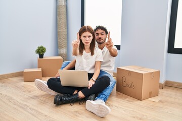 Wall Mural - Young couple using laptop at new home pointing with finger up and angry expression, showing no gesture